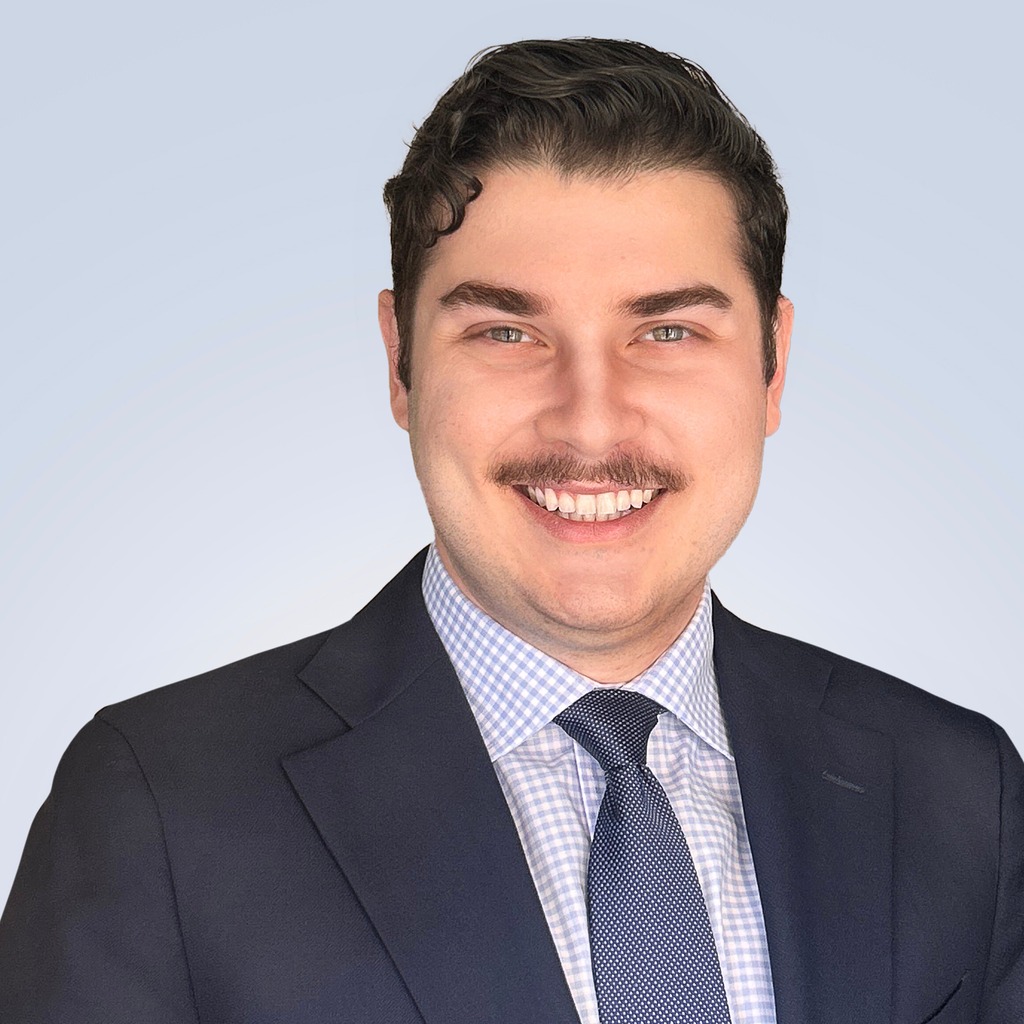 19. Investment banking MD. Smiling man in a dark suit and patterned tie, set against a light blue gradient virtual background