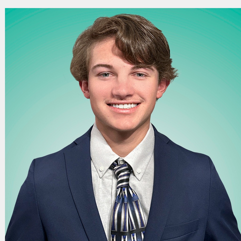 27. AmLaw partner. Young man in a navy suit and patterned tie, smiling against a solid teal background. AmLaw default