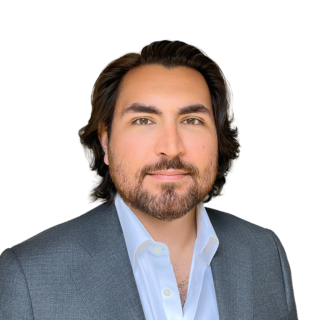 34. Luxury real estate agent. Man with a beard, wearing a grey suit jacket and white shirt, against a plain white background. Sotheby’s tier