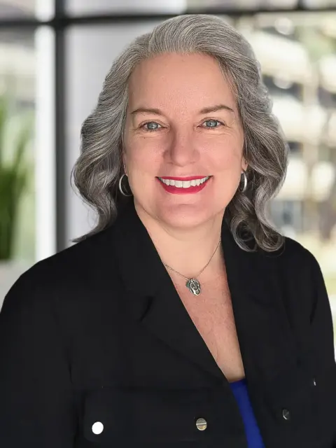 A woman with gray hair wearing a blue shirt.