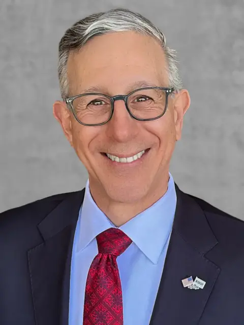 A smiling man with glasses and a red tie, exuding confidence and professionalism.