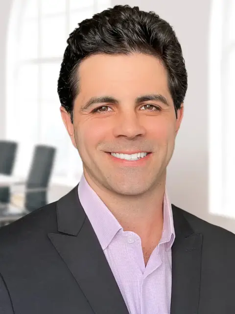 A man in a suit and pink shirt smiling, radiating confidence and happiness.