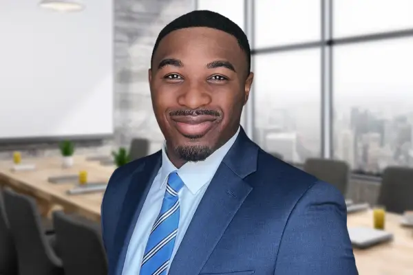 A professional black man in a suit and tie standing confidently in front of a large window.