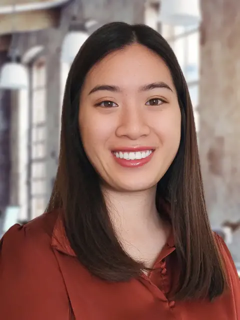 A woman with long brown hair and a red shirt standing confidently.