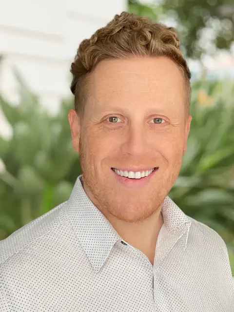 A man with curly hair wearing a white shirt.