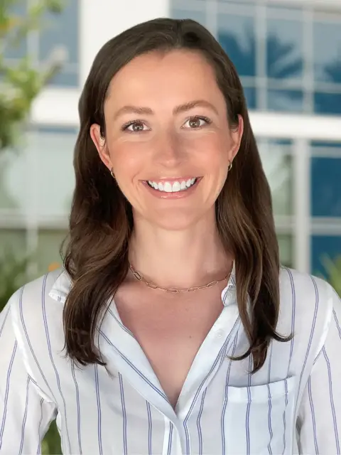 A woman with long brown hair wearing a white shirt.